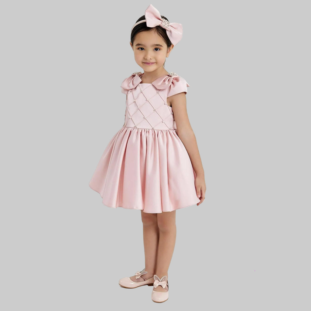 Young girl wearing a pink dress with ruffled sleeves and a matching headband on a white background