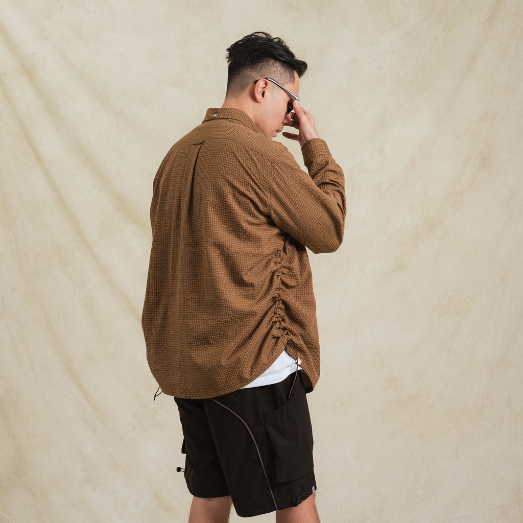 Man wearing a brown textured shirt and black shorts against a beige background