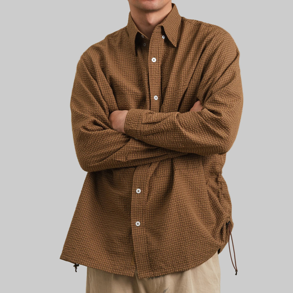 Person wearing a brown checkered shirt against a beige background
