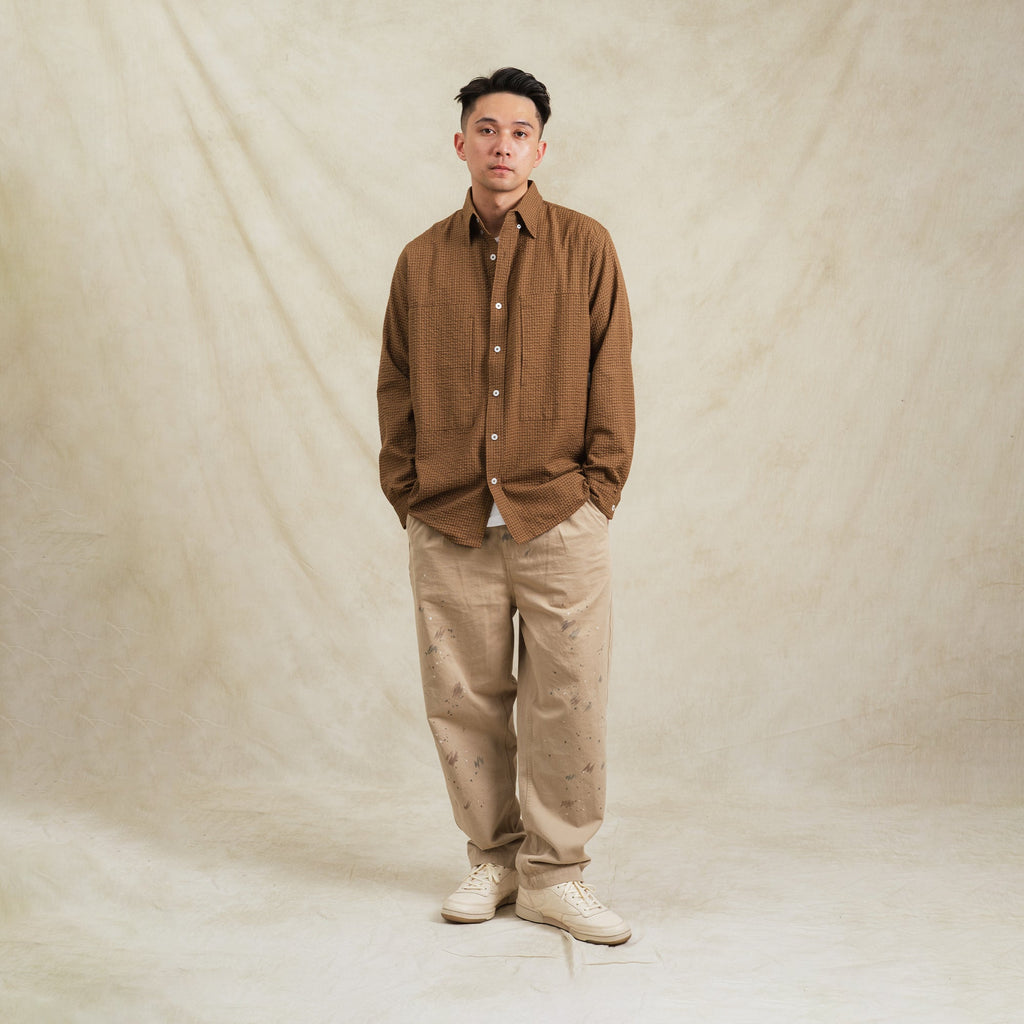 Man wearing a brown shirt and beige pants against a plain background