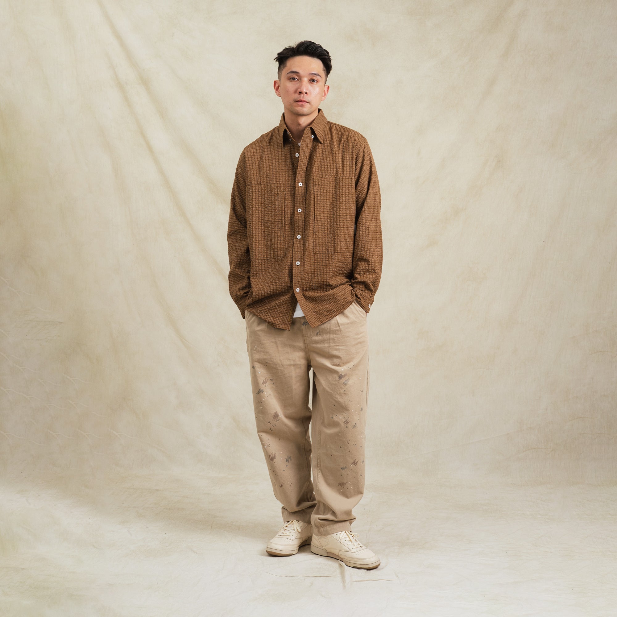 Man wearing a brown shirt and beige pants against a plain background